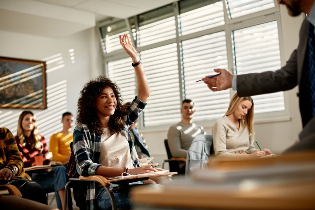 college student raising hand in classroom, for article about community college