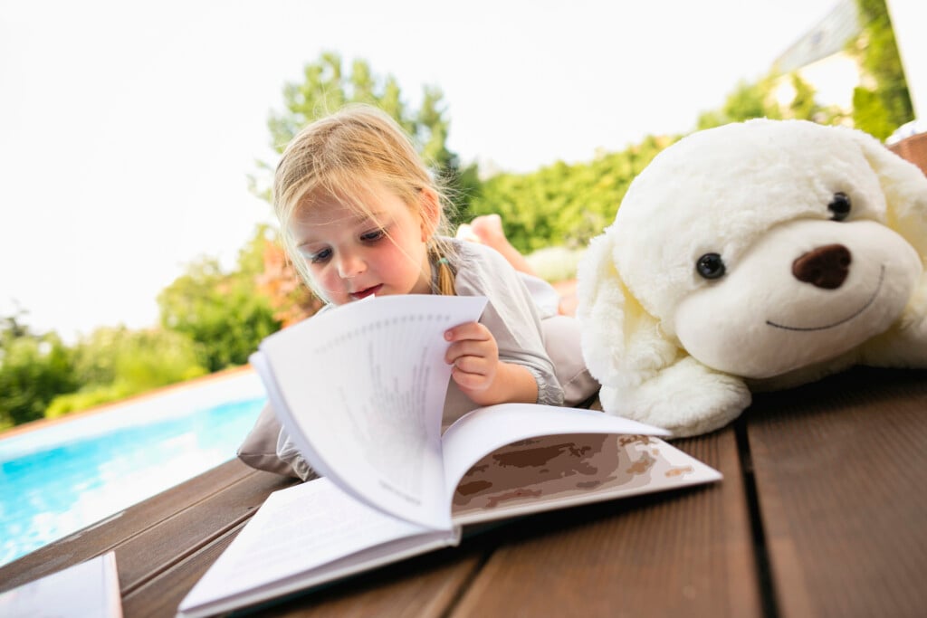 Young Girl Reading Book By Swimming Pool