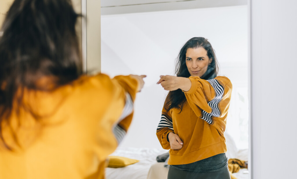 woman pointing at herself in the mirror, for article. on positive image