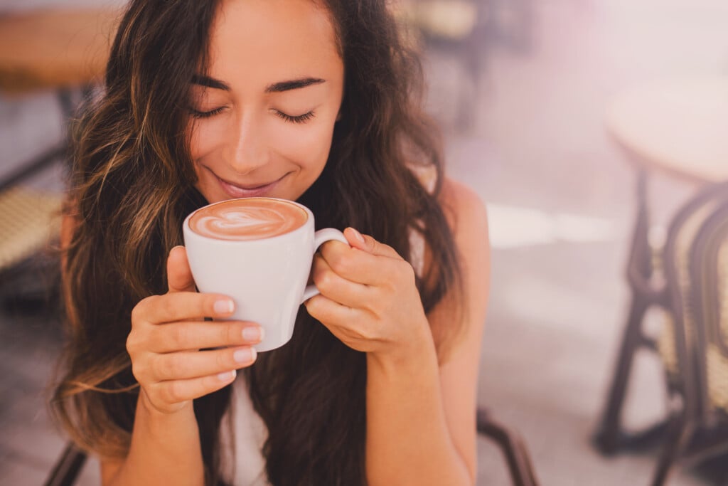 woman smiling into a latte mug, for article on luxuries for moms
