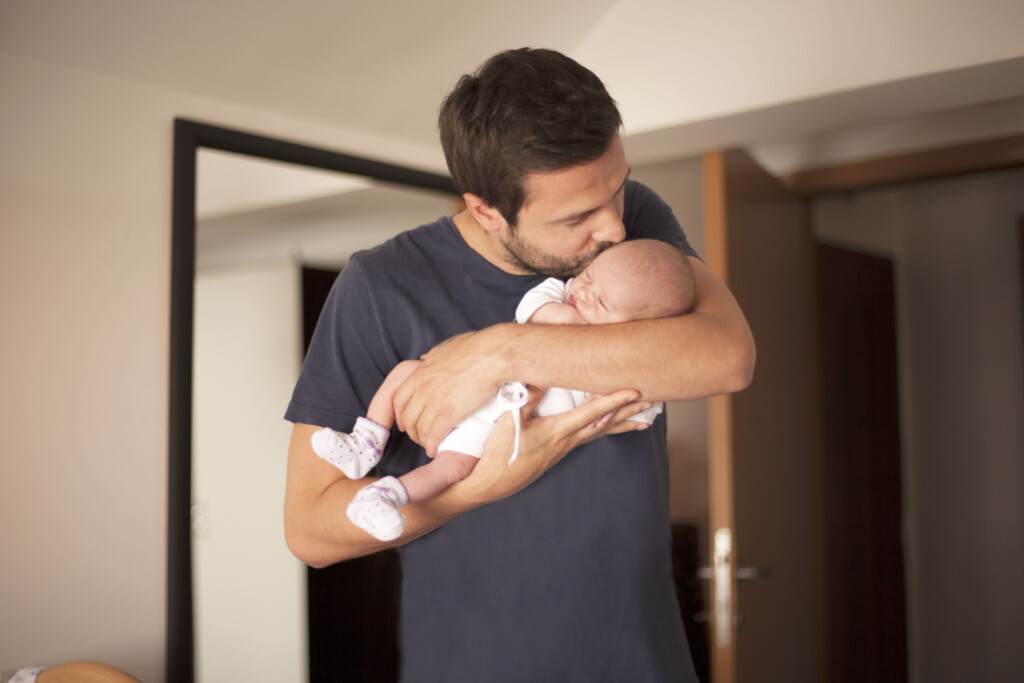 dad kisses newborn baby, for article on default parenting