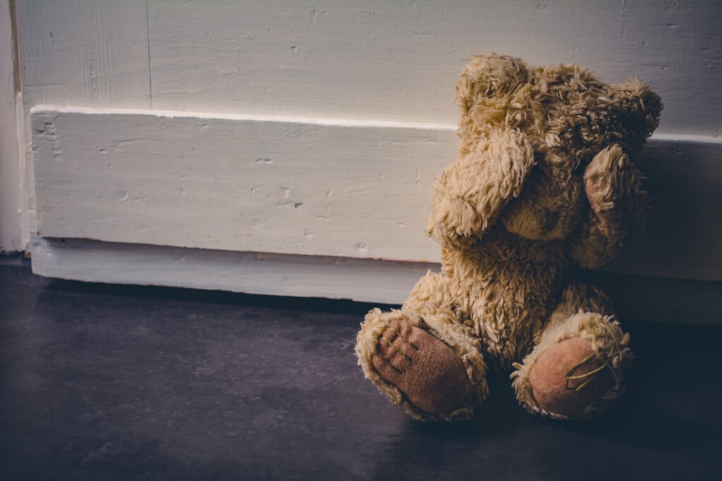 Abandoned Teddy Covering His Eyes, Sitting At A Door - child abuse concept for article on munchausen by proxy