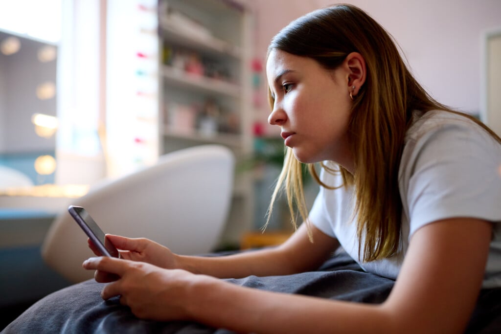 teenage girl looking at smartphone, for article on social media legislation for teens