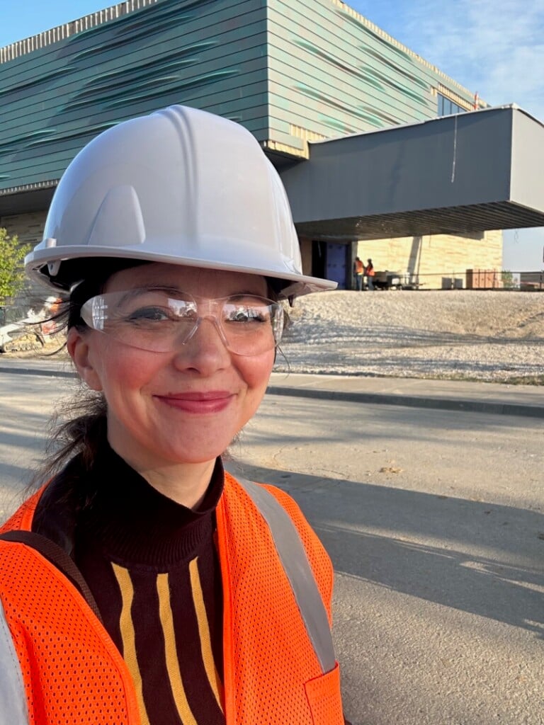 tara rittler stands in front of the new gilcrease museum building wearing hard hat and safety gear