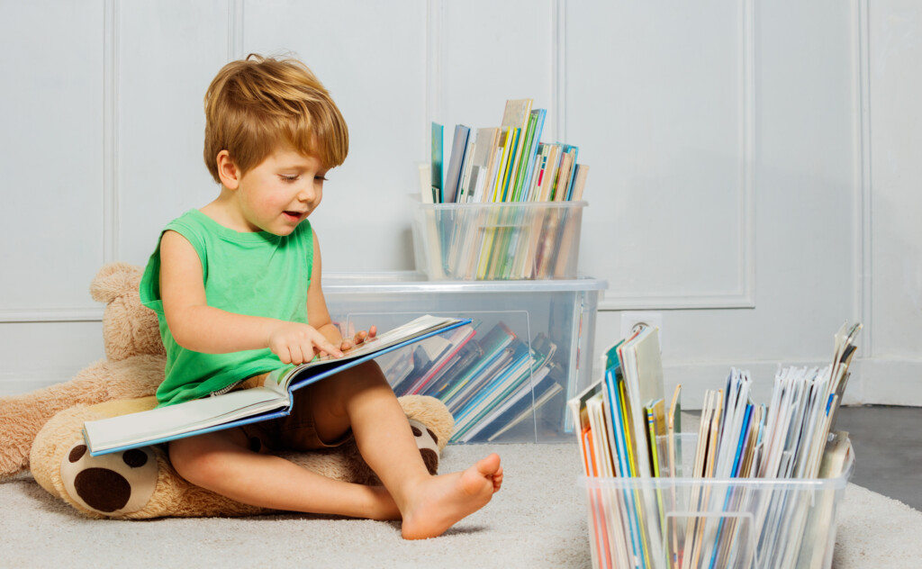 Boy Reading Text, Sitting On White Carpet Amidst Many Book Boxes