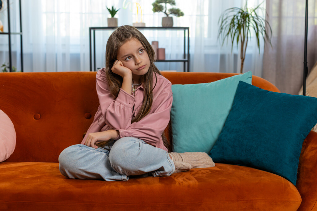 preteen girl sitting on couch looking bored