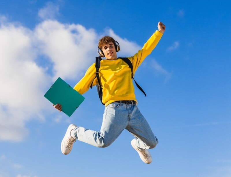 Happy College Student Jumping With Headphones And Binder