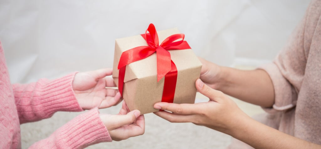 a young child's hands and an adults hands, with a wrapped gift in between