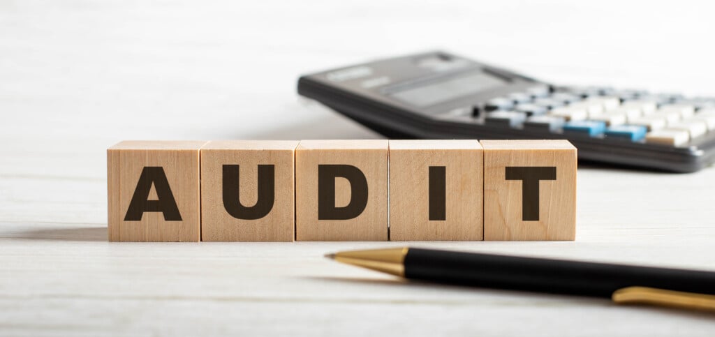 The Word Audit Is Written On Wooden Cubes Between A Pen And A Calculator.