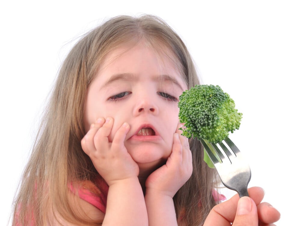 a girl making a disgusted face at a piece of broccoli