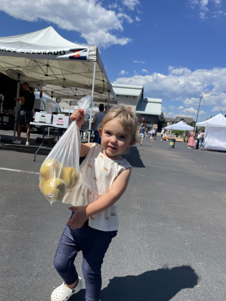 a young girl holding a bag of apples at a farmers market