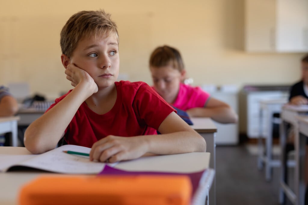 a boy at a school desk looking up and unhappy