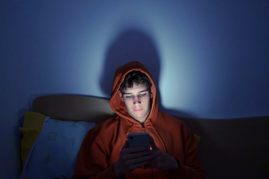 Teenager Using Smartphone Sitting On Bed At Night