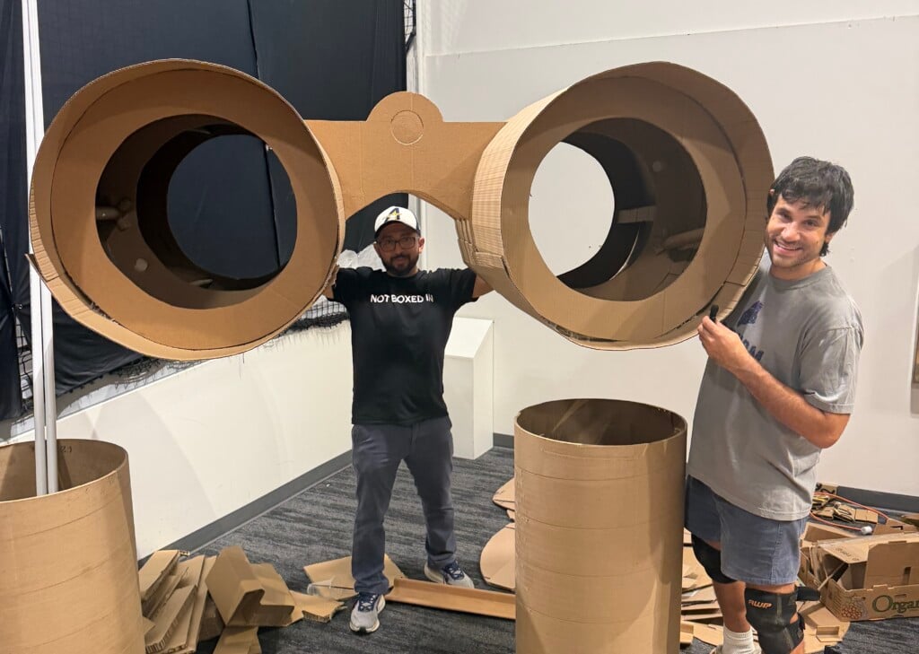 Luis Flores (Left) and Symon Hajjar (Right) holding a giant pair of binoculars made out of cardboard