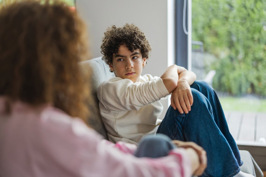 teen sits on couch and looks at mother with anxious expression