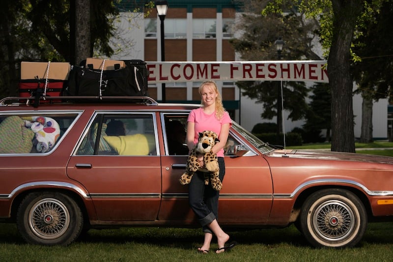 girl stands in front of old car full of stuff, for article on leaving for college