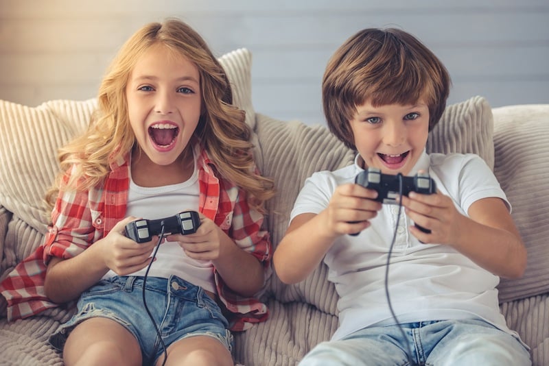 a girl and a boy sitting on couch playing video games. summer screen time concept