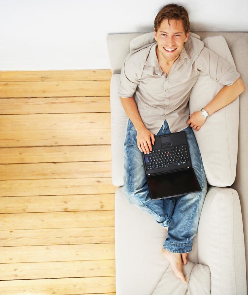 male college student on a coach in a dorm room with a laptop, for a dorm room checklist