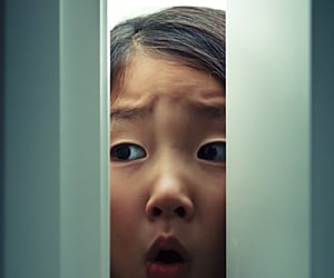 scared girl peeking through door, for article on childhood fears