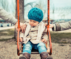 child playing on swing with two adult hands on either side. divorcing parents concept