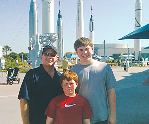 a father and two sons stand in front of the kennedy space center