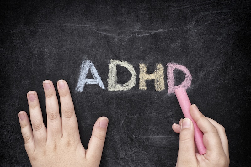 small hands writing adhd on a chalkboard. children with adhd concept