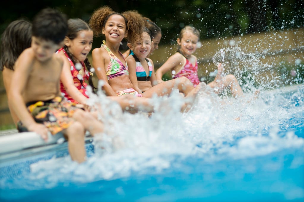 group of kids on the side of a pool, smiling and splashing