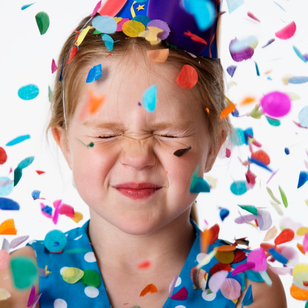 girl in party hat squinting as confetti rains down. for our list of resources for birthday parties in tulsa