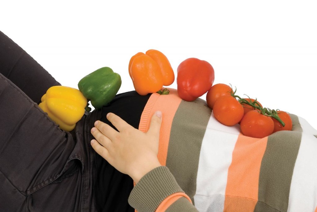 pregnant woman with vegetables on her belly, for article on pregnancy diet