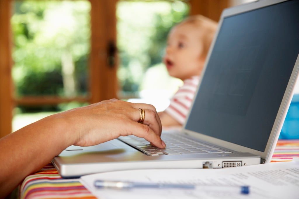 adult using laptop with baby in background, for article on oversharing on social media