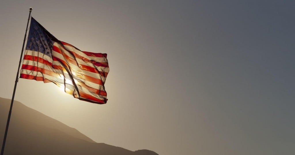 Back-lit American flag flying on pole with copy space.