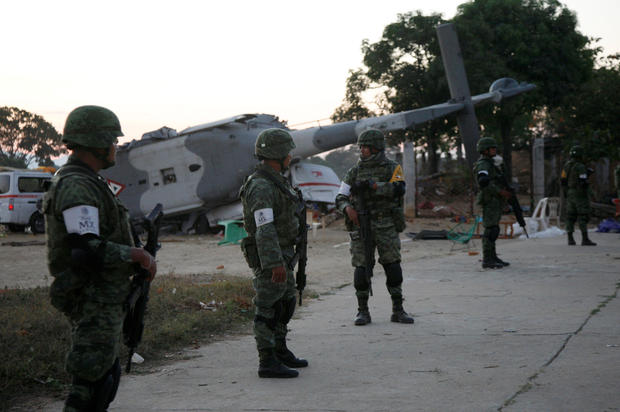 Soldiers stand guard next to a military helicopter