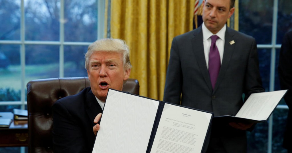 U.S. President Donald Trump holds up the executive order on withdrawal from the Trans Pacific Partnership after signing it as White House Chief of Staff Reince Priebus stands at his side in the Oval Office of the White House in Washington January 23