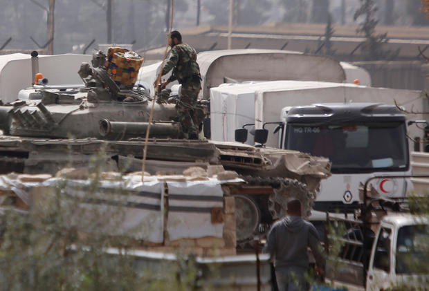 Red Crescent trucks are seen parked near Syrian soldiers at a checkpoint near Wafideen camp in Damascus
