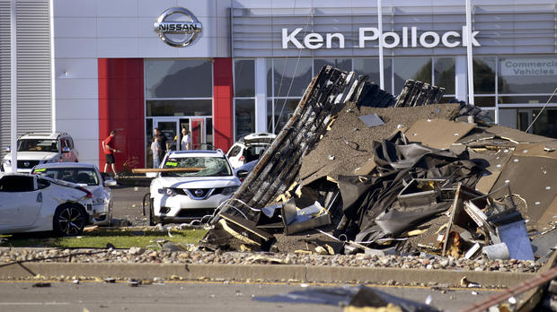 Debris and damaged vehicles sit in front of a car dealership on Thursday