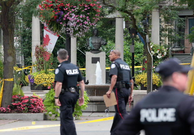 Police officers walk past Alexander the Great Parkette while investigating a mass shooting on Danforth Avenue in Toronto