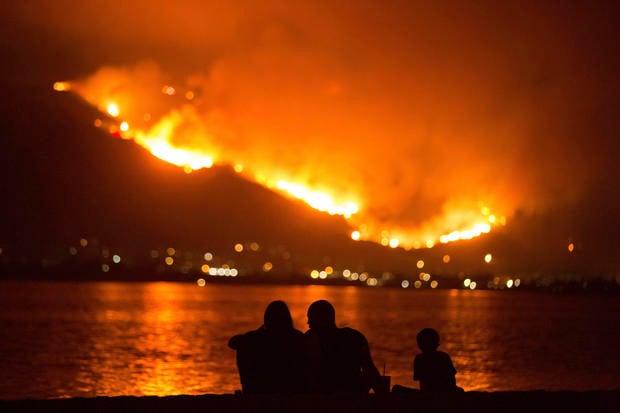 A family sits along the shore of Lake Elsinore as they watch the Holy Fire burn in the distance on Thursday night