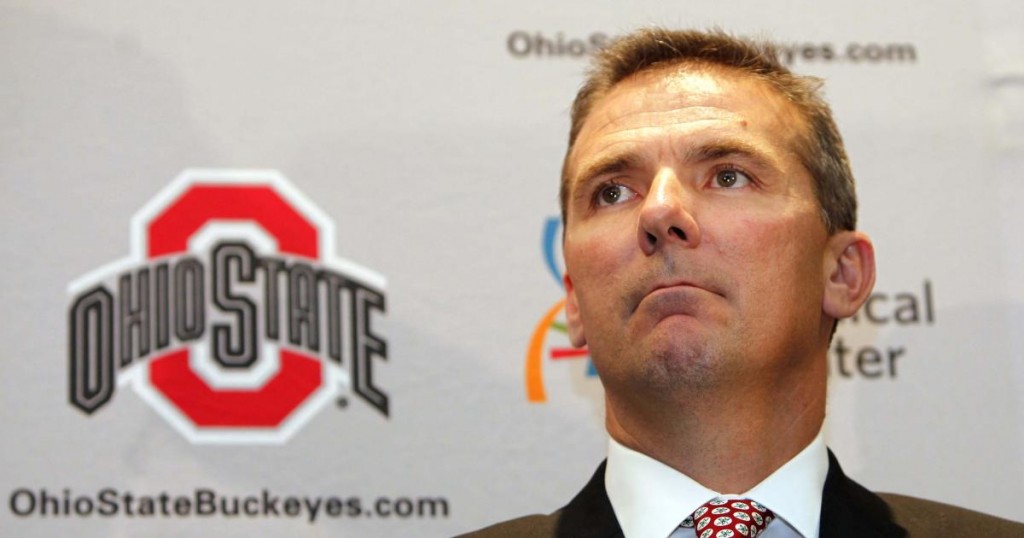 Urban Meyer listens as Ohio State athletic director Gene Smith introduces him as the new football coach at Ohio State