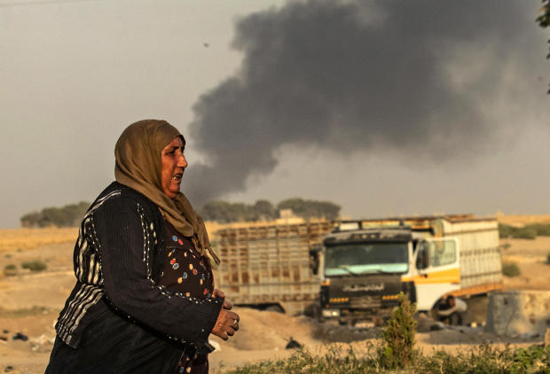 TOPSHOT - A woman walks as smoke billows following Turkish bombardment in Syria's northeastern town of Ras al-Ain in the Hasakeh province along the Turkish border on October 9