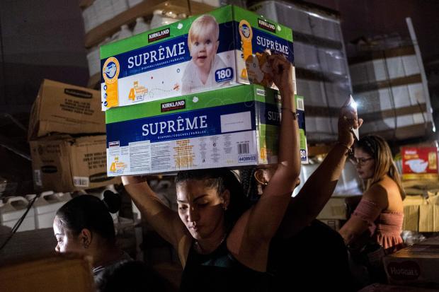 A woman carries boxes of baby diapers from warehouse filled with supplies