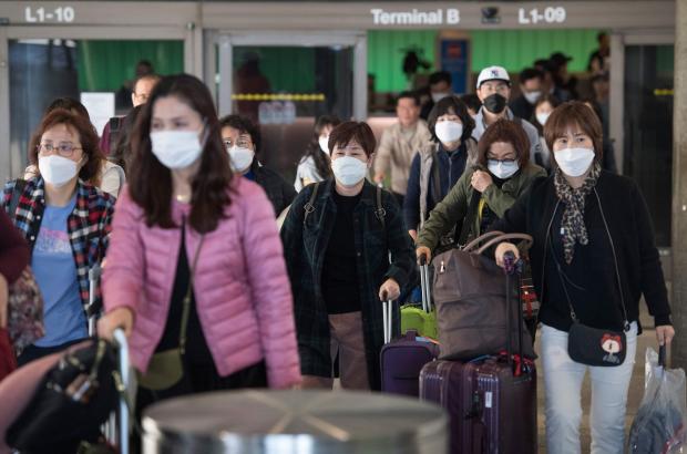 Passengers wear protective masks to protect against the spread of the Coronavirus as they arrive on a flight from Asia at the Los Angeles International Airport