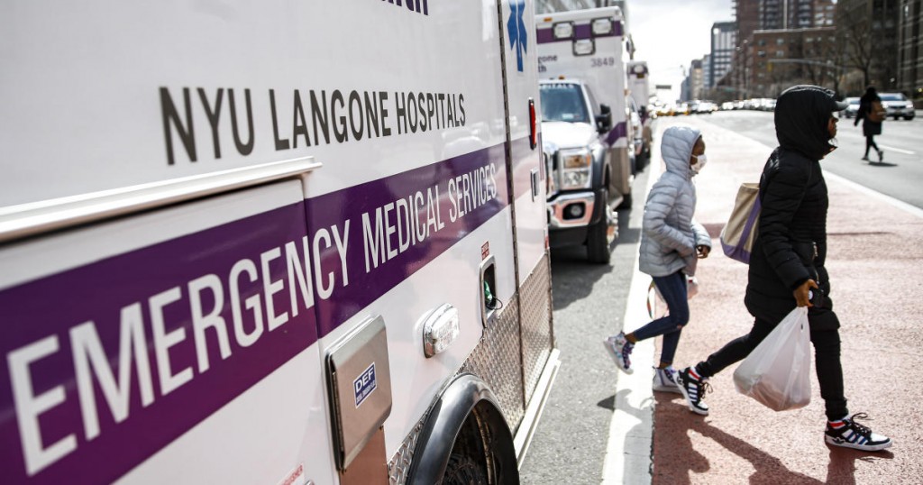 A pedestrian wearing a protective face mask walks past a line of ambulances outside the NYU Langone Hospital Emergency room entrance