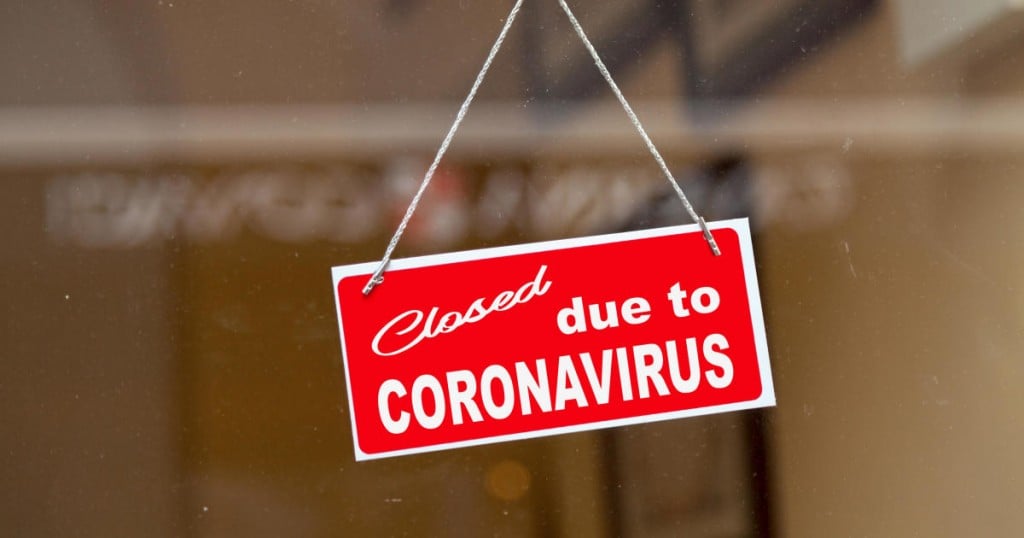 Red sign hanging at the glass door of a shop saying "Closed due to coronavirus".