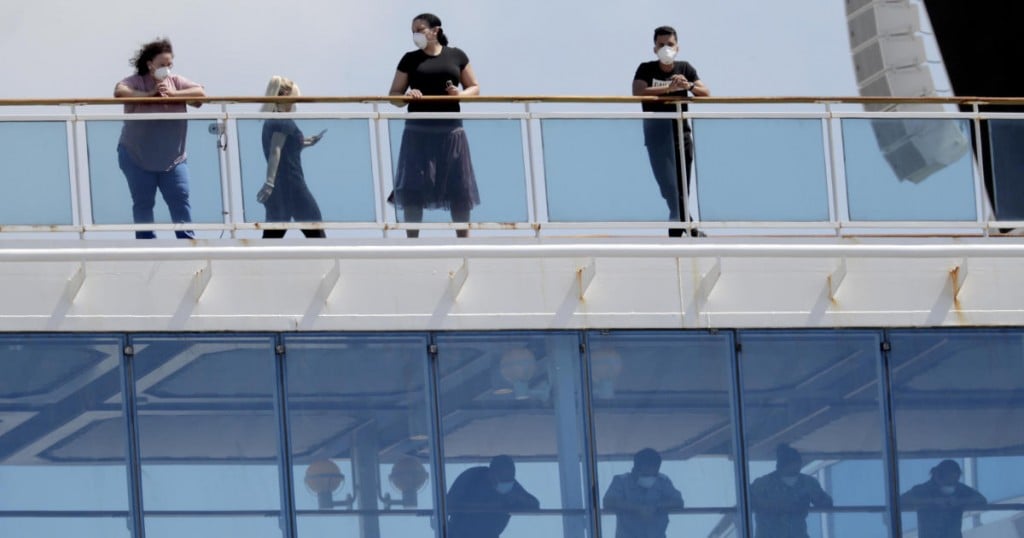 People wearing protective masks look out from the Coral Princess cruise ship while docked at PortMiami during the new coronavirus outbreak