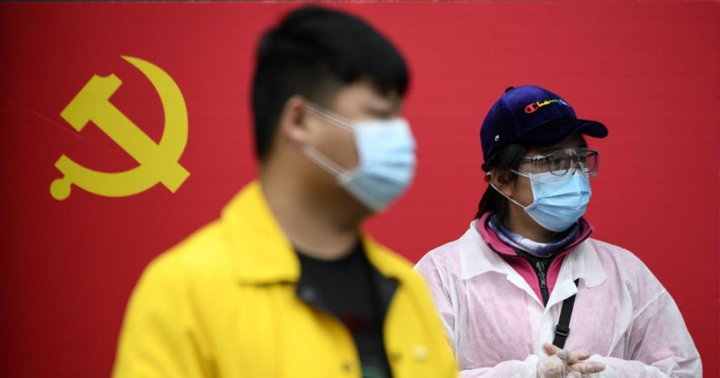 People wearing face masks stand in front of a Communist Party of China flag along a street in Wuhan