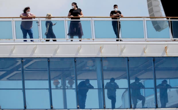 People wearing protective masks look out from the Coral Princess cruise ship while docked at PortMiami during the new coronavirus outbreak