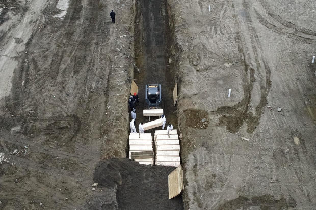 Workers wearing personal protective equipment bury bodies in a trench on Hart Island