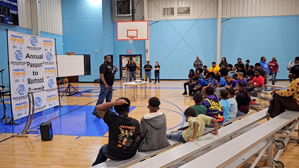 Boys And Girls Club Gymnasium With Kids On Bleachers Watching A Speaker