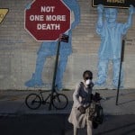 A Woman Wearing A Mask Crosses The Street In Front Of A Mural About Traffic Accidents Reading, 