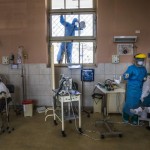 A Worker Wearing Protective Gear Cleans A Window As A Nurse Tends To A Patient Inside The Intensive Care Unit For People Infected With The Coronavirus